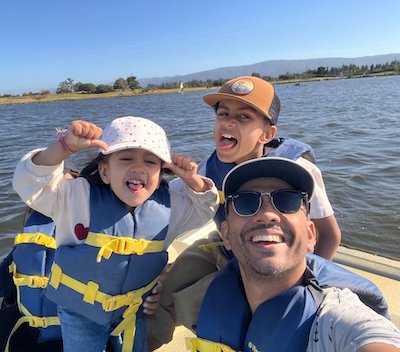 Rajat on a boat with his two kids, all three grinning at the camera